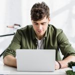 handsome architect in green shirt sitting at table with laptop in office